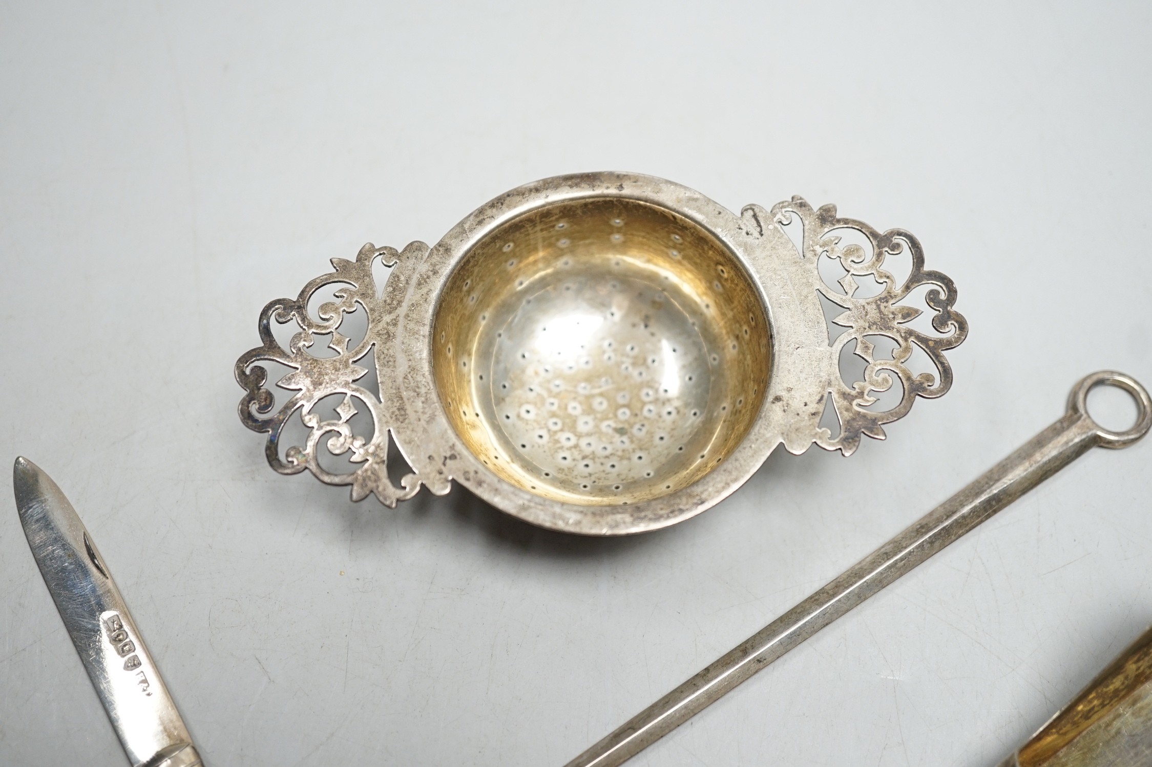 A silver tea strainer, a George III silver 'shovel' caddy spoon, London, 1811, a mother of pearl handled silver fruit knife and George IV silver game skewer, London, 1825, 14.7cm.